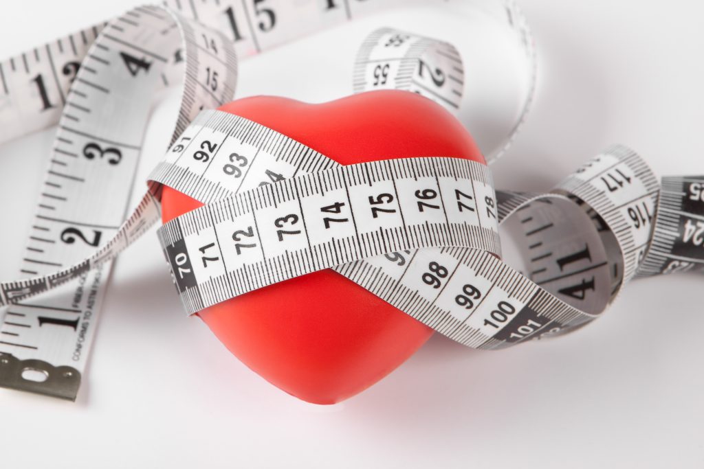 Red heart wrapped with a white measuring tape symbolizing health, fitness, and heart care.