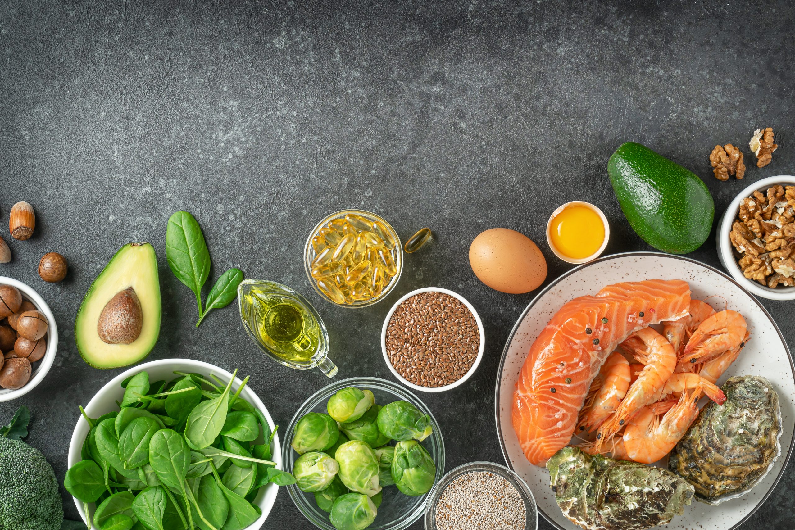 A selection of nutrient-dense foods suitable for both paleo and keto diets, featuring avocados, leafy greens, nuts, seeds, salmon, shrimp, eggs, and healthy oils. This image showcases the natural, whole foods emphasized in the paleo diet vs keto debate.
