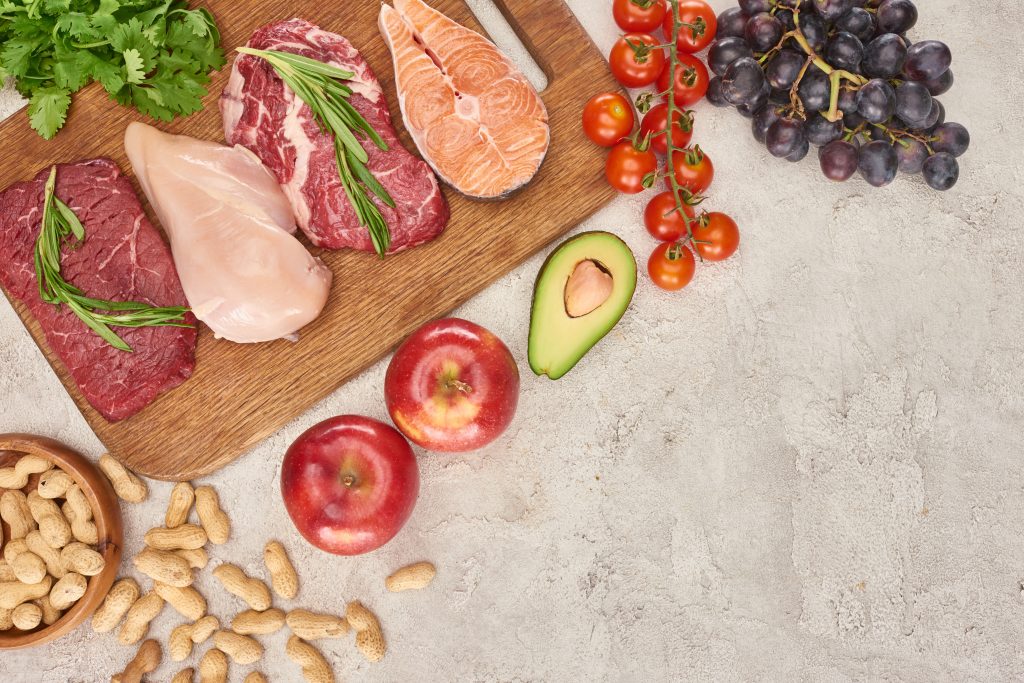 A top view of an assortment of meats, poultry, and fish, accompanied by fresh fruits, vegetables, and nuts. This diverse selection of foods emphasizes the nutritional variety available in the difference between paleo and keto diet, highlighting the whole, unprocessed foods central to both dietary approaches.