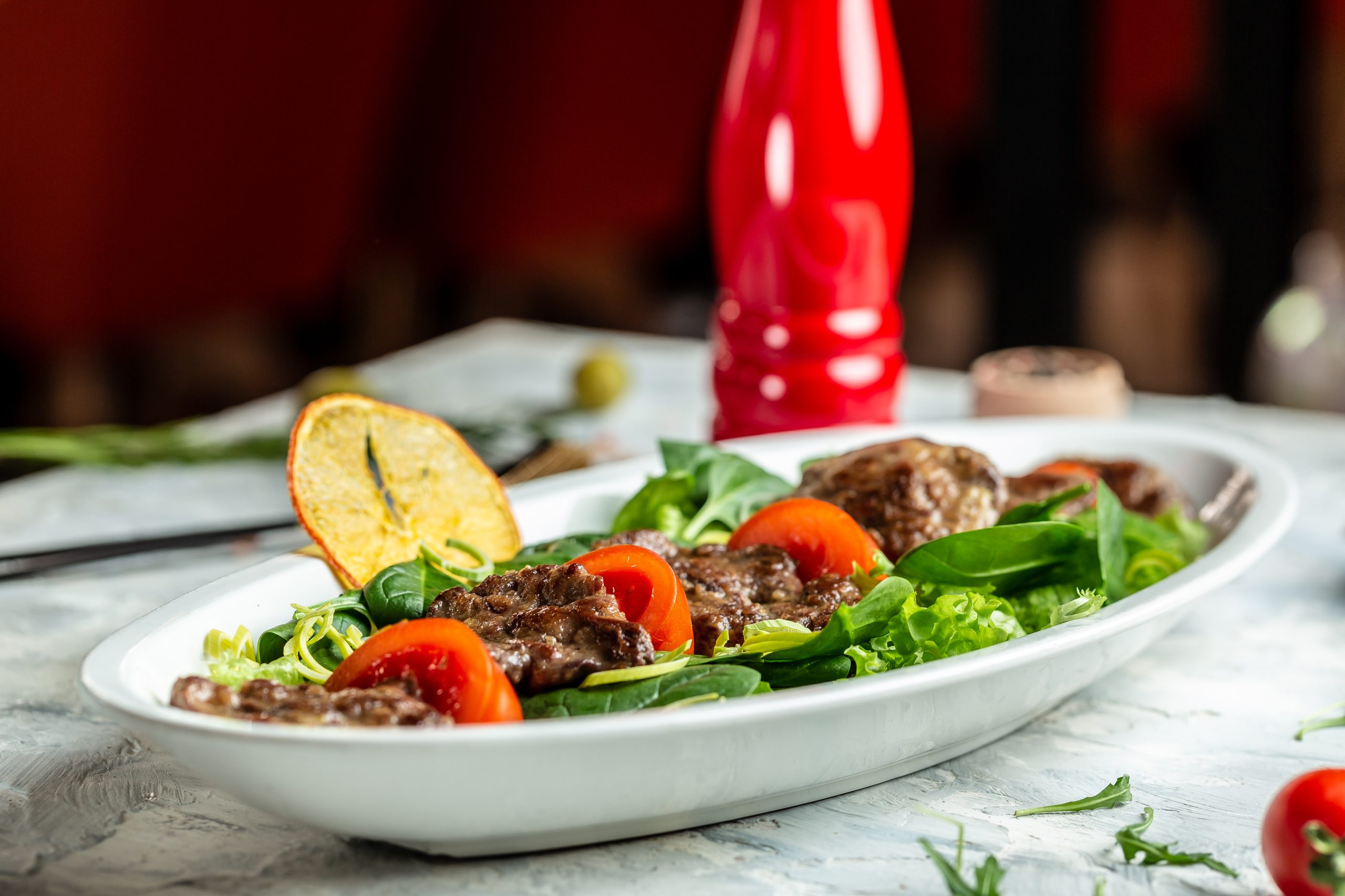 A healthy and vibrant South Beach Diet recipes featuring a baby spinach salad with tender beef liver and fresh tomato slices, garnished with a lemon slice and dressed in balsamic reduction.
