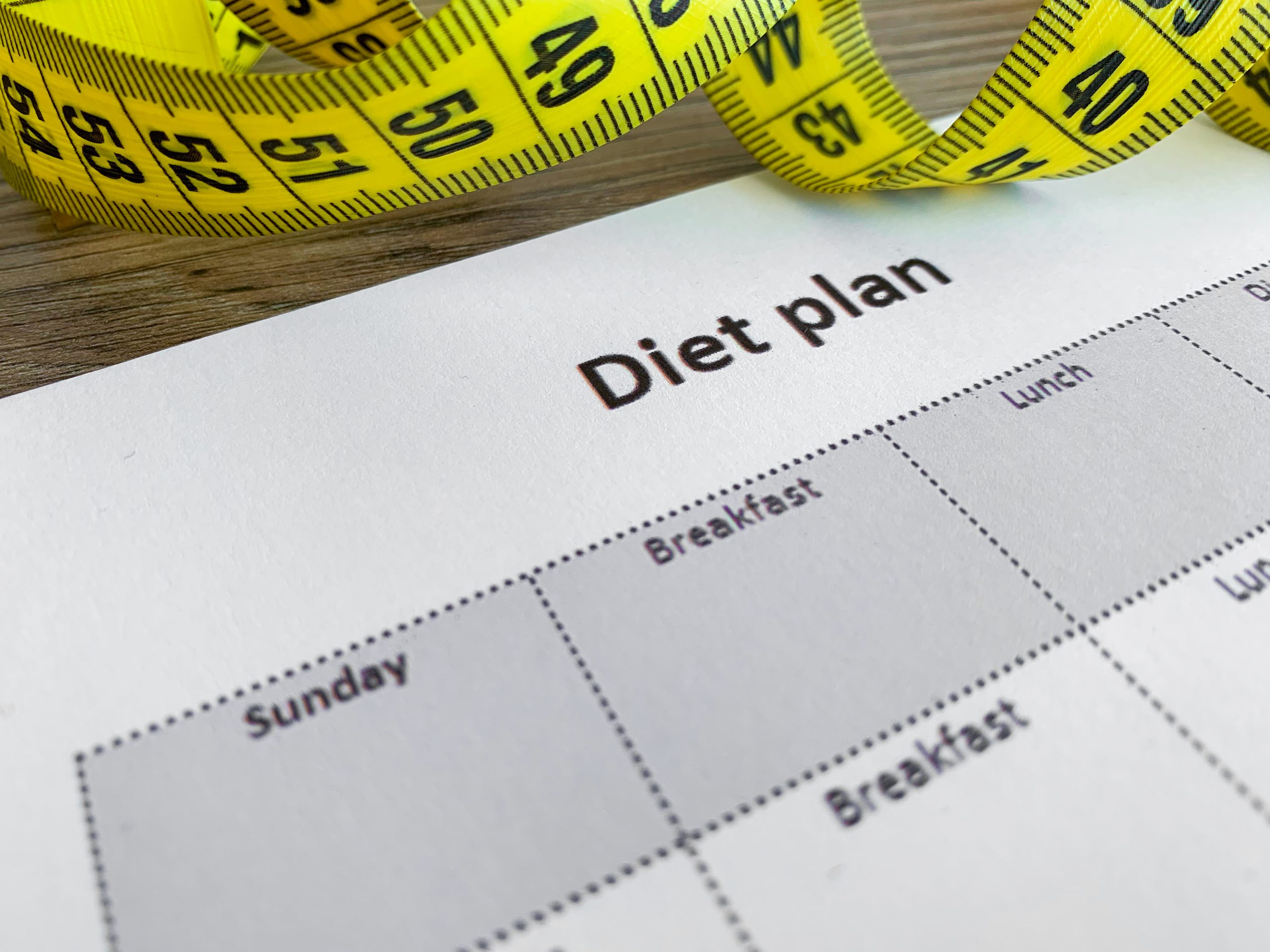 Diet plan concept. Measuring tape and diet plan on wooden background.