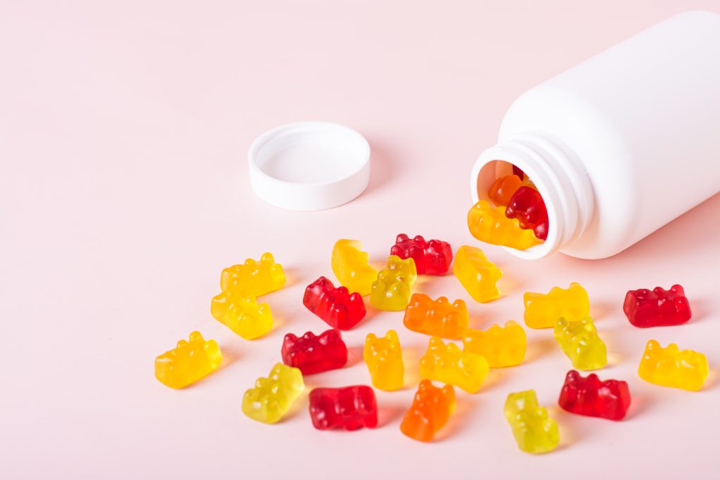 Colorful gummy candies spill from a white bottle onto a pink background, illustrating a playful approach to the keto gummy diet. These bear-shaped treats offer a sugar-free option suitable for dietary restrictions.