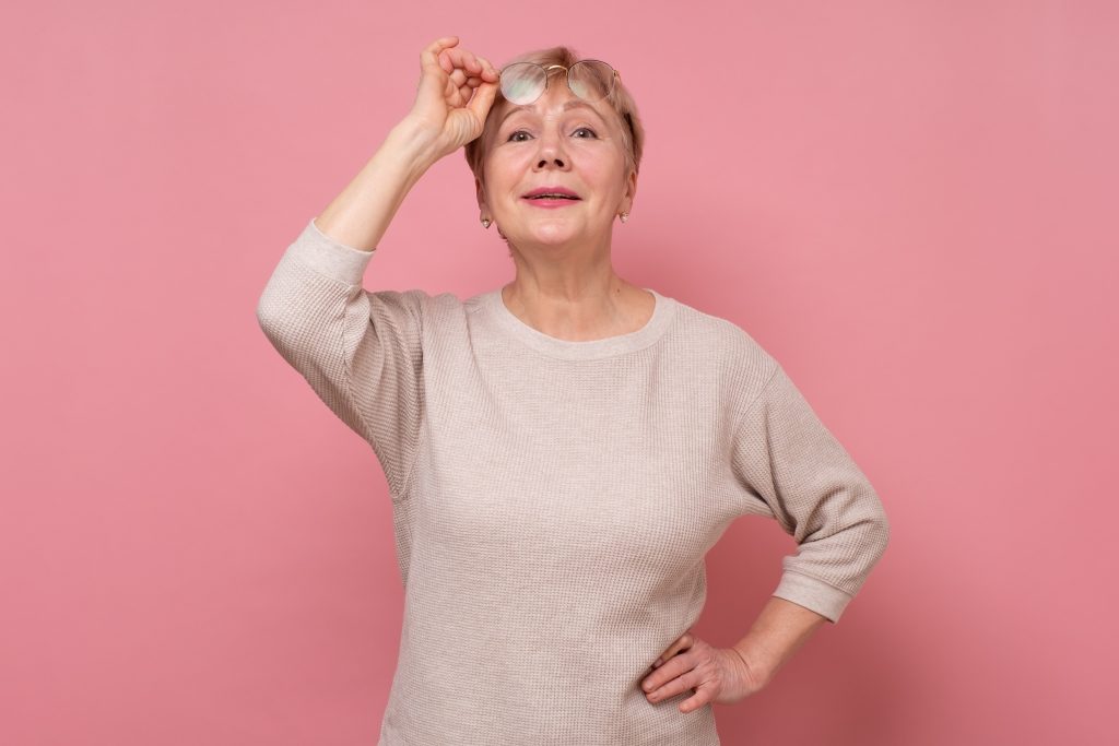 Happy joyful senior lady looking at camera and smiling isolated on pink background