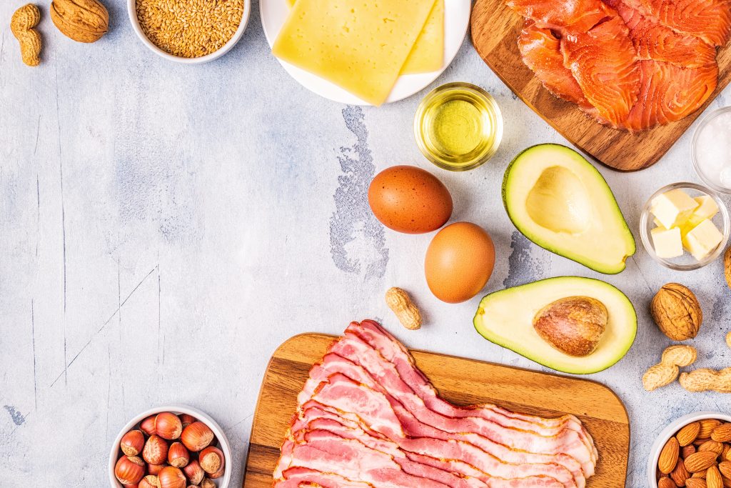 Selection of healthy foods for South Beach Phase 2, featuring bacon, avocado, nuts, cheese, eggs, salmon, and seeds, arranged on a light background.