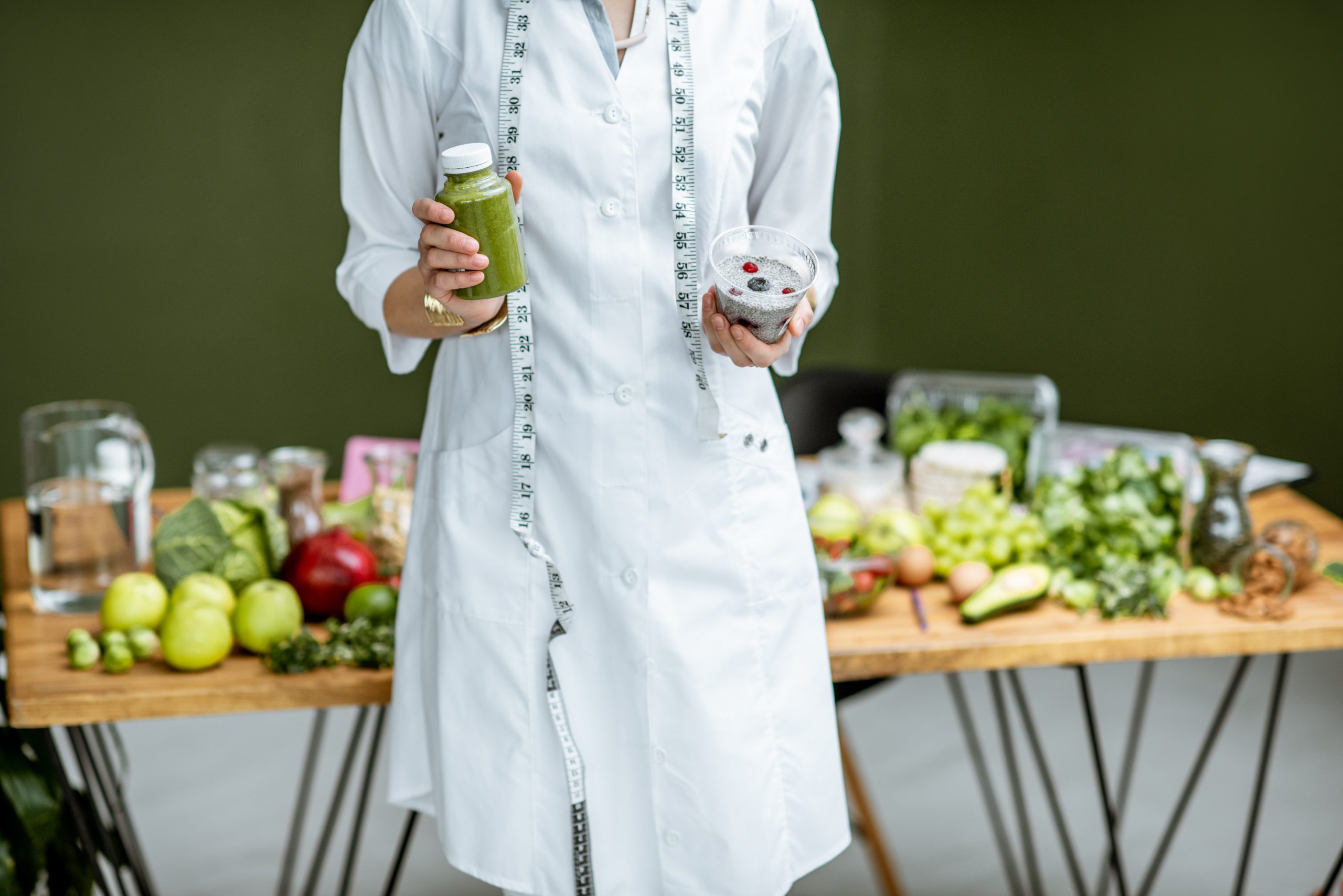 Nutritionist in medical gown holding salad and smoothie drink with healthy food on the background, close-up view with no face. Best 3-day colon cleanse for weight loss