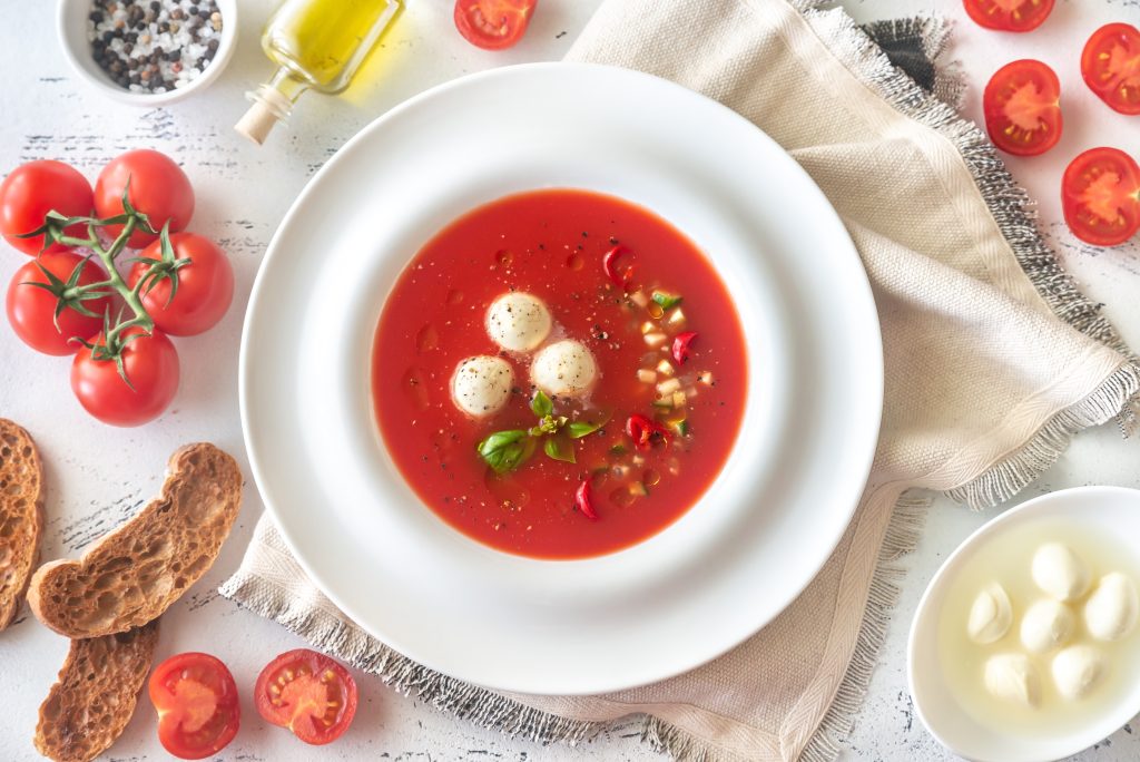 A delicious and refreshing portion of gazpacho, a classic cold Spanish soup, served with fresh tomatoes, mozzarella balls, and a drizzle of olive oil, perfect for a healthy South Beach Diet meal.