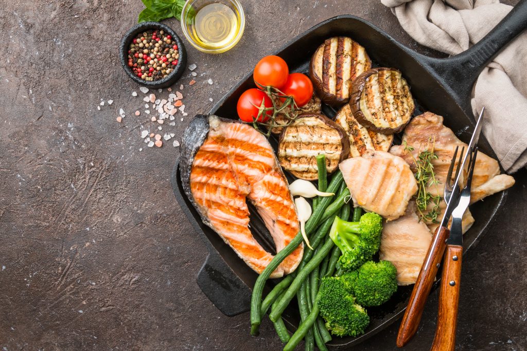 healthy food - grilled salmon steak, chicken and vegetables over dark background, top view